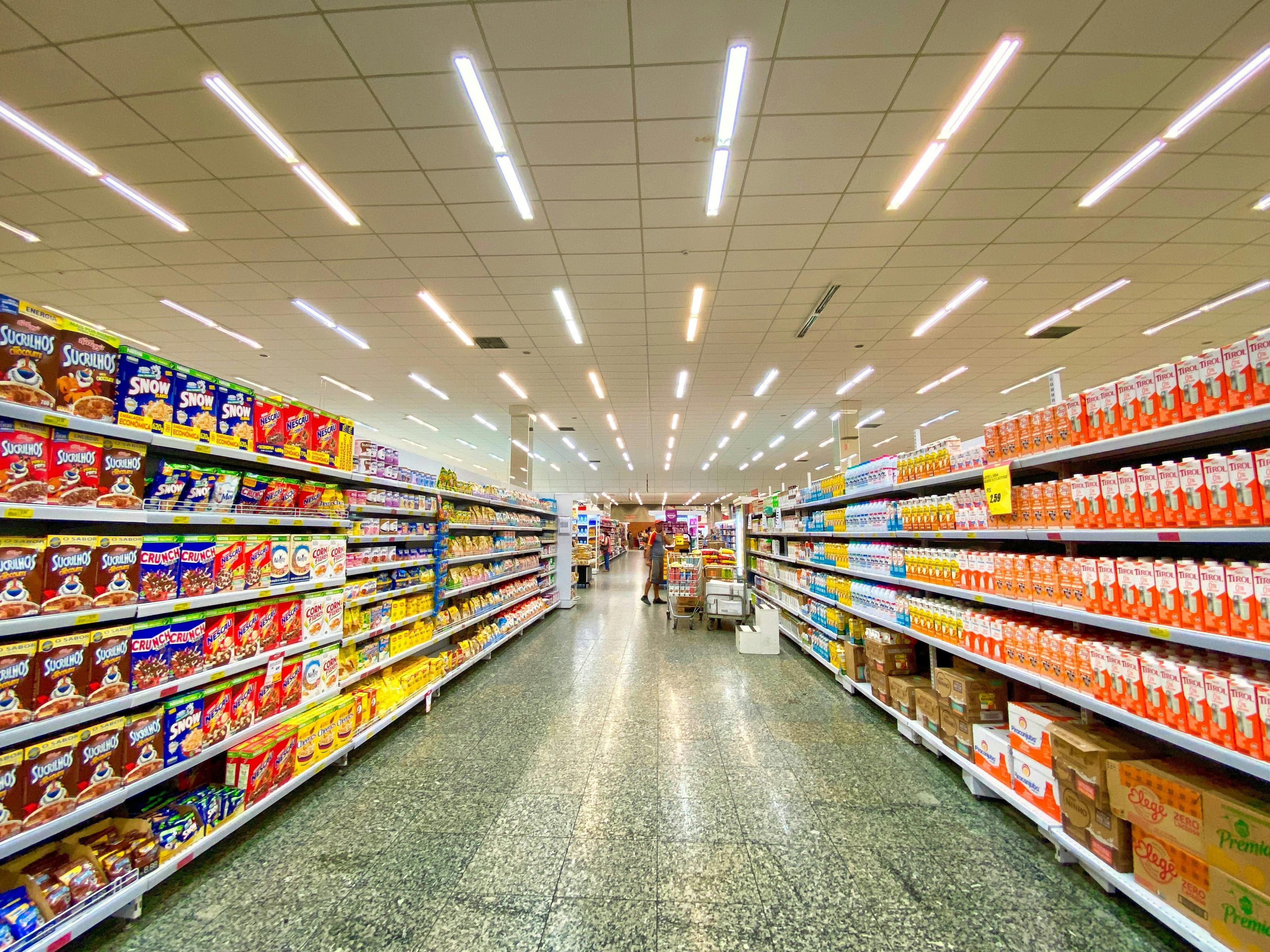 A long, brightly lit grocery store aisle with shelves full of various products.