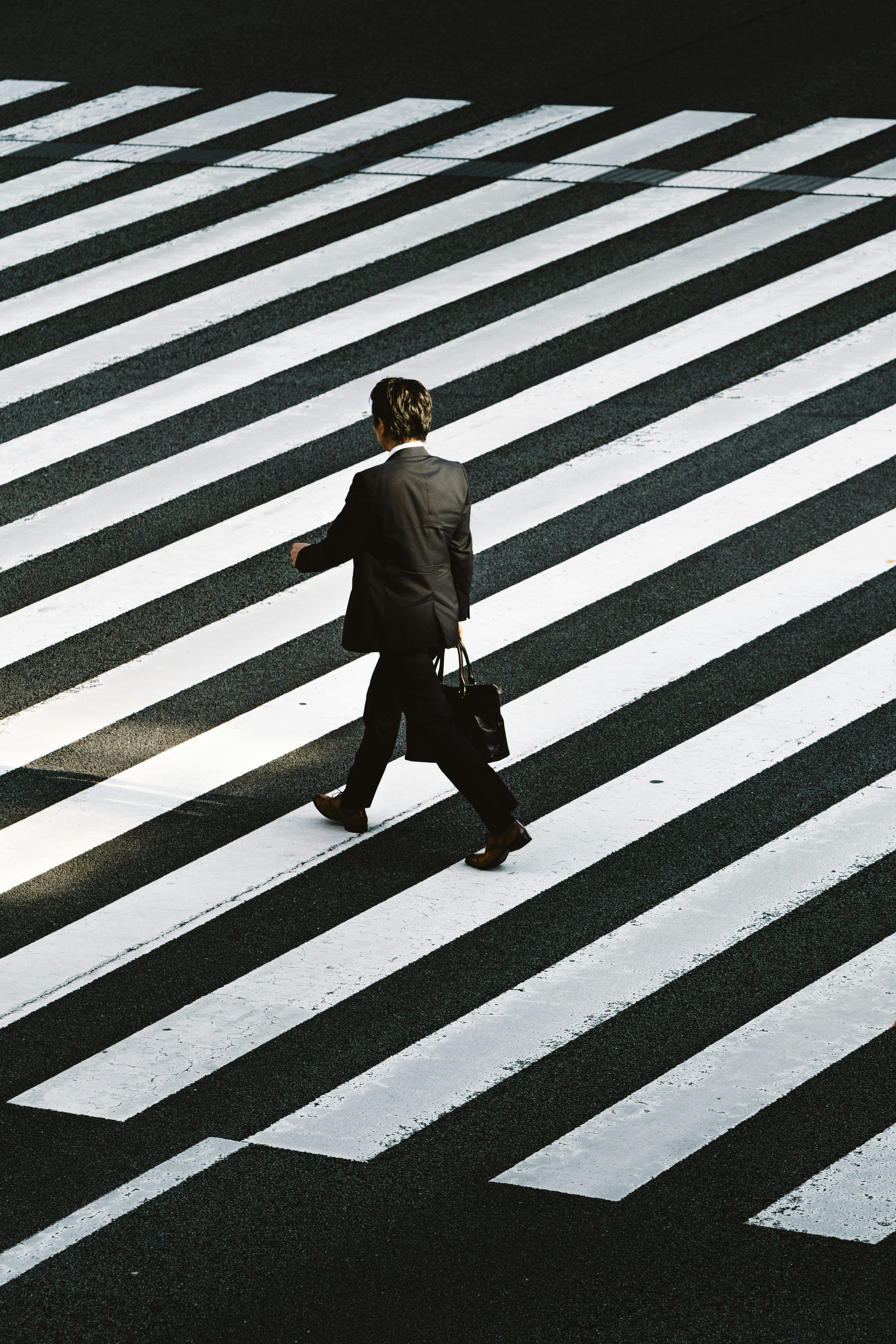 Man in suit walks across a zebra crossing with strong shadows.
